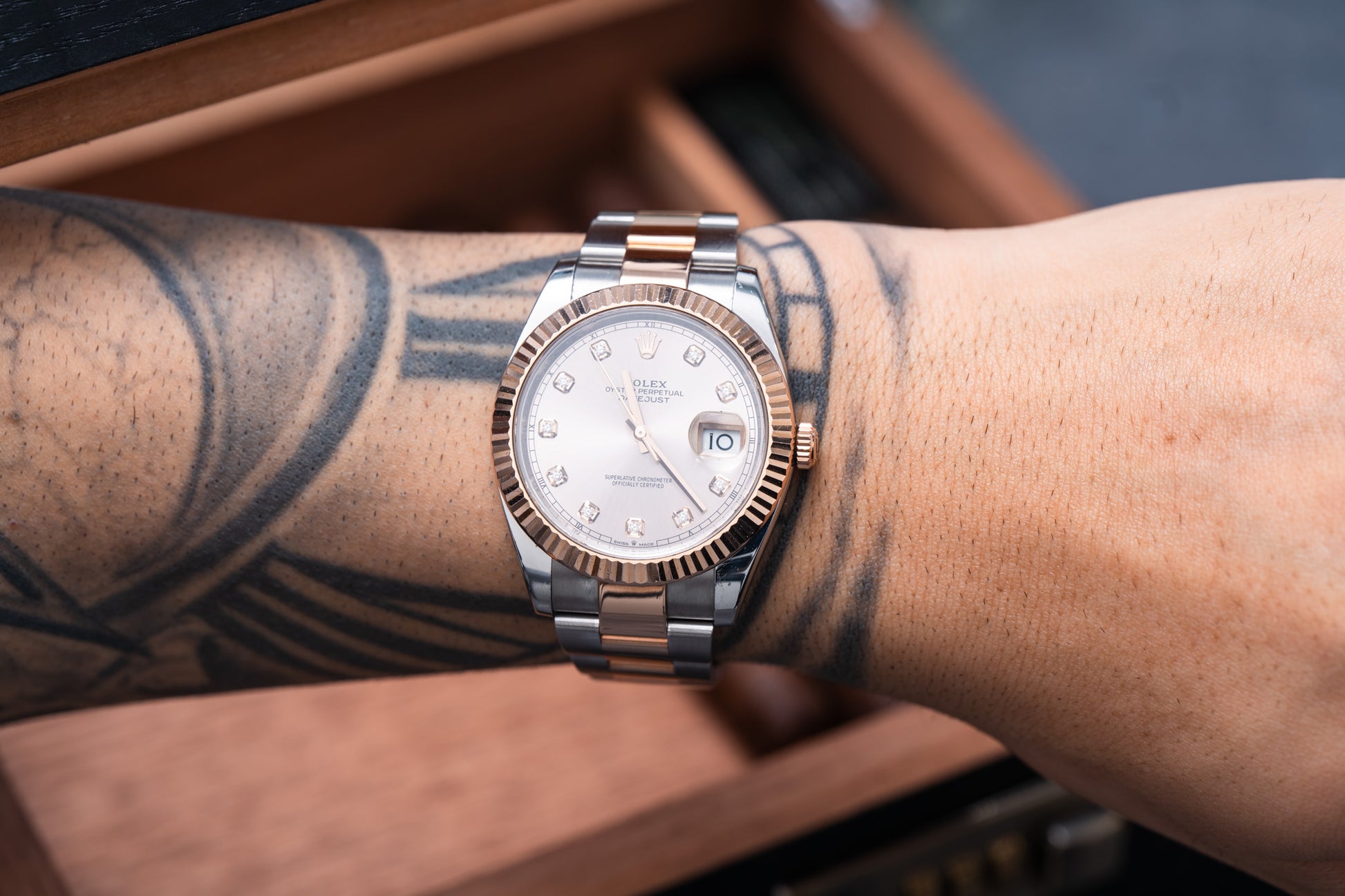 Rose gold watch on a wrist with tattoos, blurred background